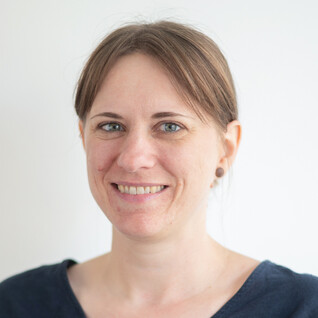 Frau mit braunen Haaren, Zopf und Lächeln.